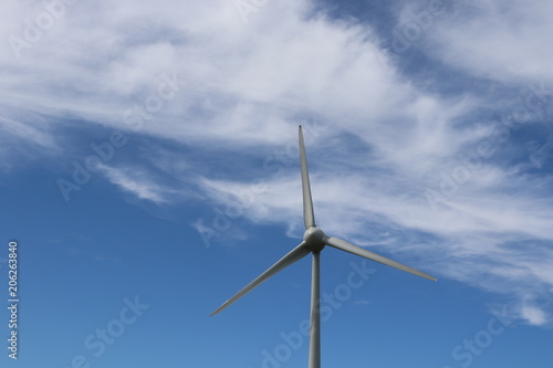 Close up of wind turbine in blue sky with fluffy white clouds © mcKensa