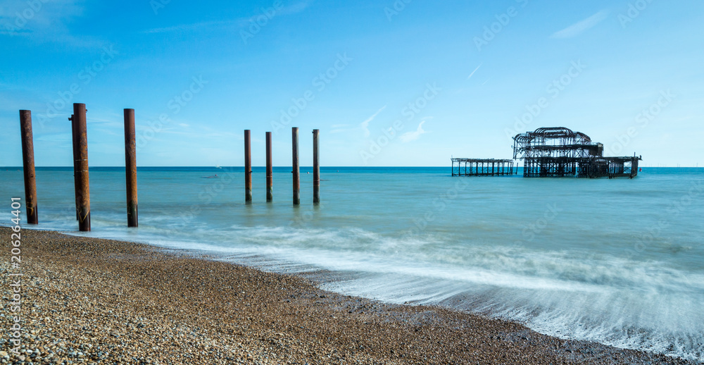 Old Brighton Pier seen from the pebble beach with the waves rolling in on a sunny day