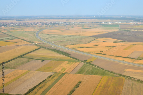 Plains with different crops and plants, highway and a city suburb seen from a landing plane