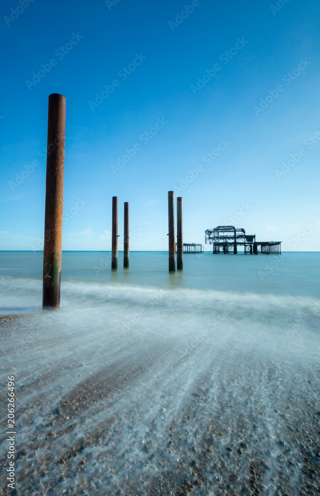 Old Brighton Pier seen from the pebble beach with posts in the foreground and waves rolling in