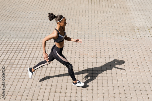 Young woman running on street. Side view of sporty woman exercising outdoors.