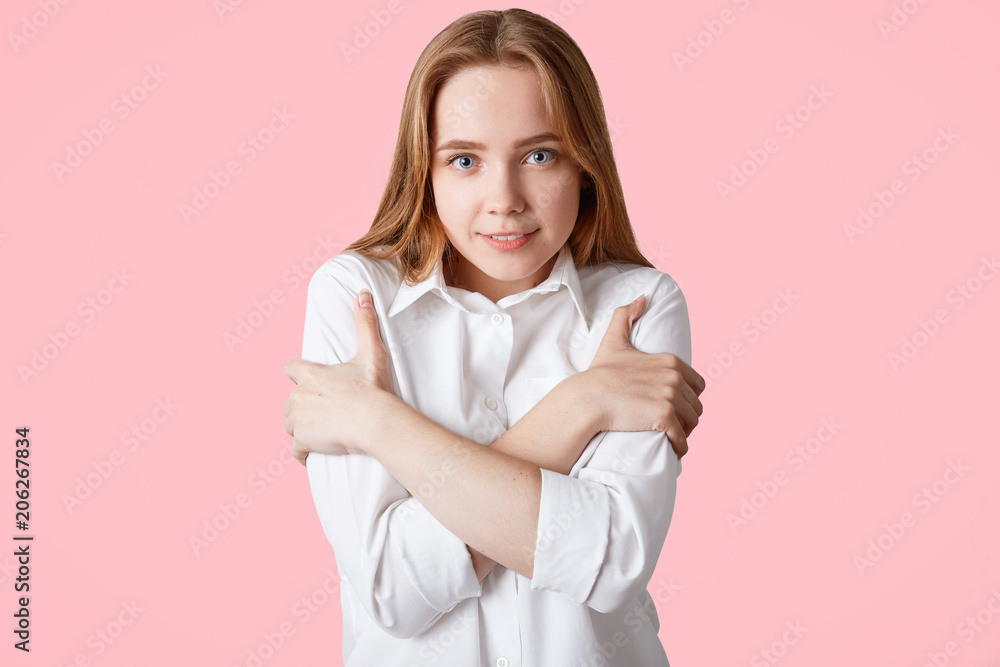 Reserved beautiful shy female with pleasant appearance, keeps hands crossed, wears white shirt, looks directly into camera, isolated on pink background. Delighted European woman in formal clothes Reserved beautiful shy female with pleasant appearance, keeps hands crossed, wears white shirt, looks directly into camera, isolated on pink background. Delighted European woman in formal clothes