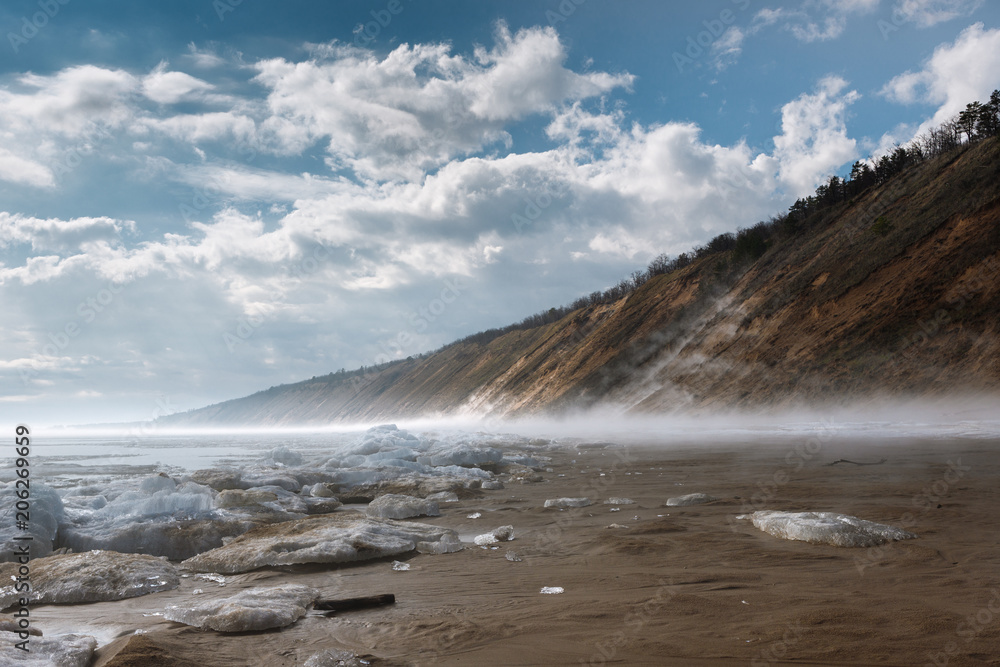 Fototapeta premium a misty spring morning on the snowy shore of a calm river overlooking the mountains