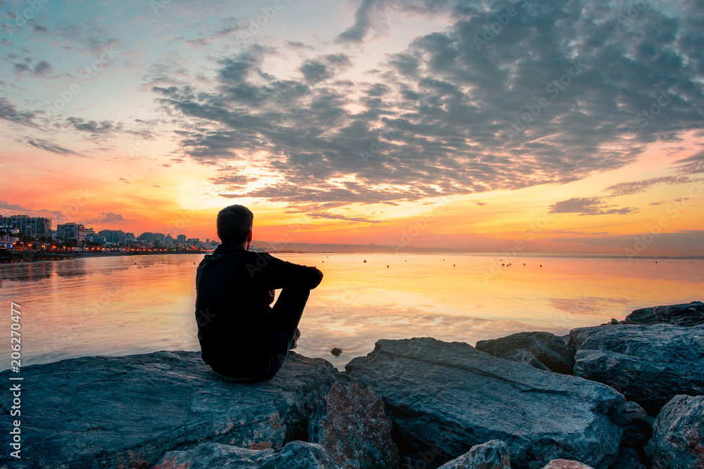 hombre joven sentado en una roca mirando el amanecer delante del mar