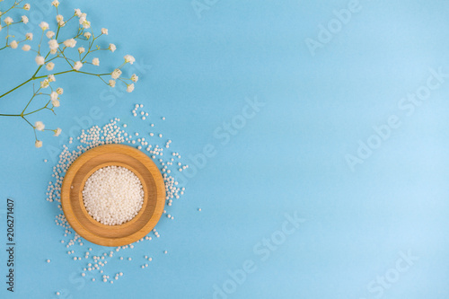 Flat lay Combined bowl with tablets and flower. Homoeopathy medical grains on a wooden plate, scattered on a table, and a green flowering branch of grass