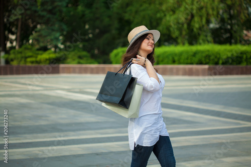 Beautiful smiling brunette girl in a hat walking down the street with packages from a store.