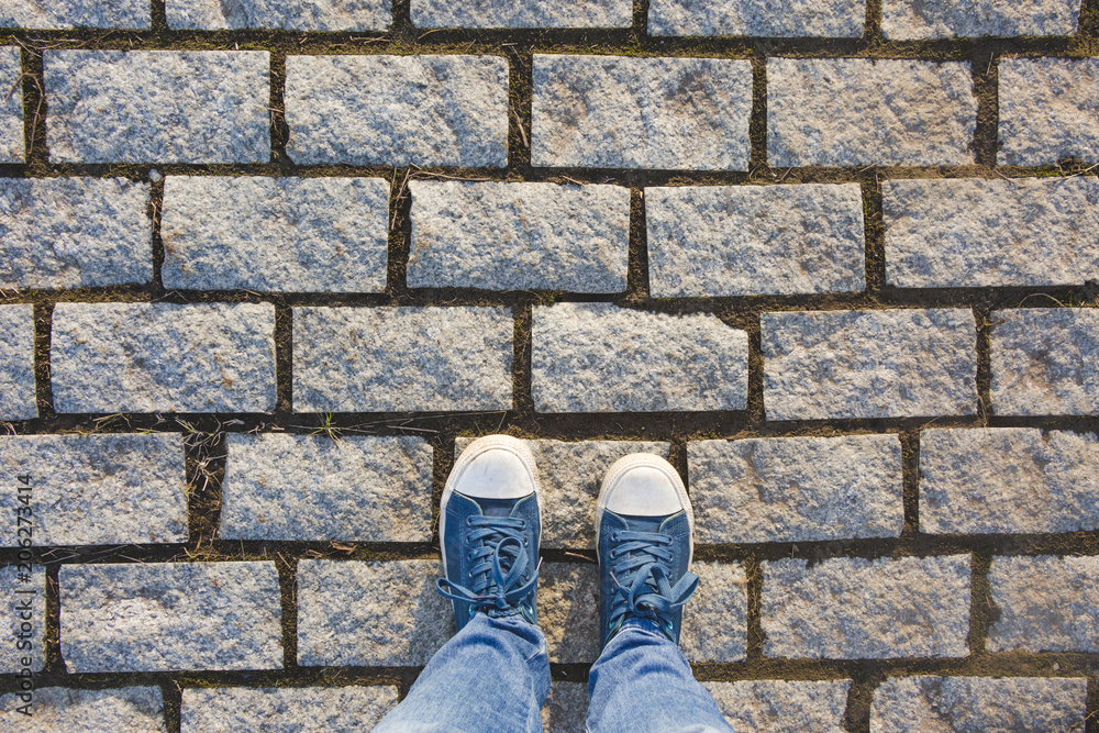 Feet in sneakers on a cobblestone pavement