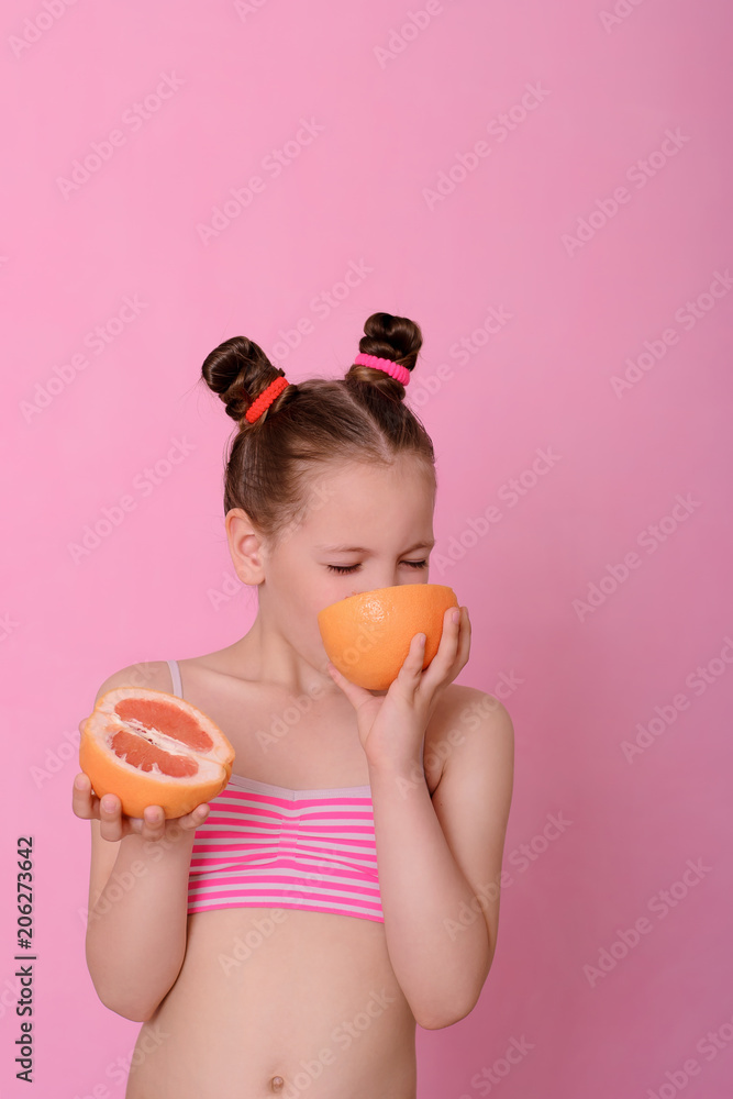 Caucasian beautiful little girl with grapefruit on a pink background Caucasian beautiful little girl with grapefruit on a pink background