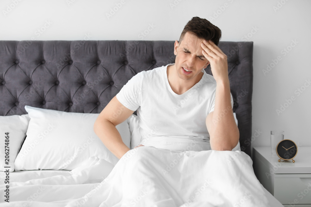 Young man with headache sitting in bed Young man with headache sitting in bed