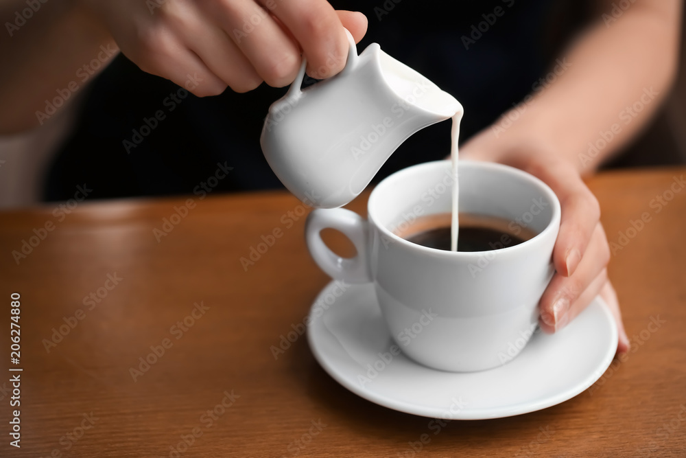 Woman pouring milk into cup of coffee on table Woman pouring milk into cup of coffee on table