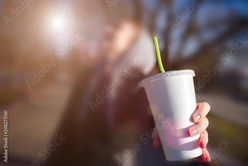 Woman drinking coffe on the street. Close up. Female hand holding a blank paper cup in a city landscape background