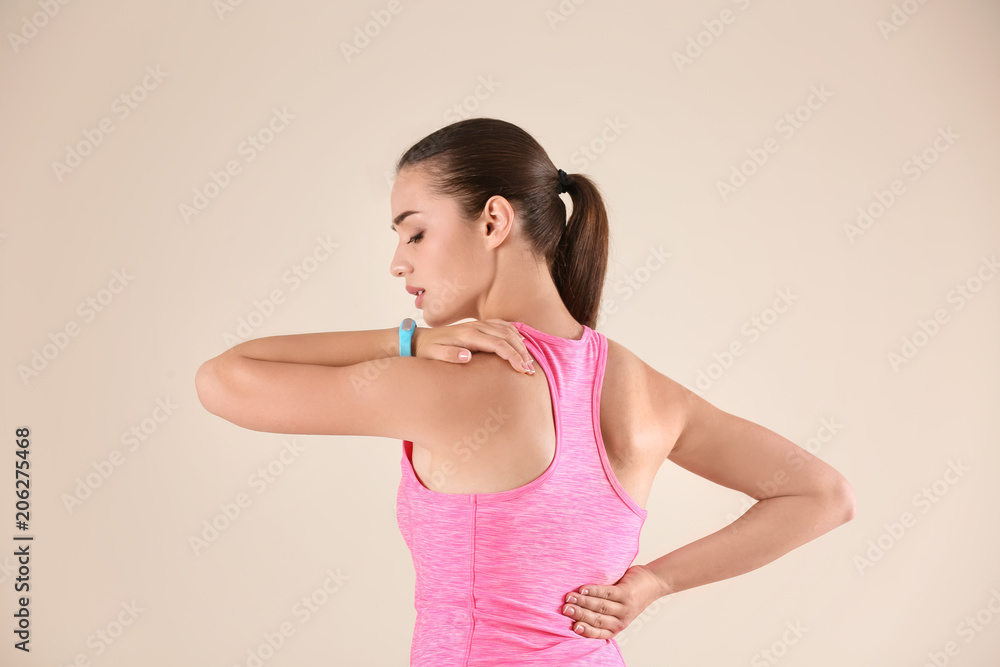 Woman in sportswear suffering from back pain on light background Woman in sportswear suffering from back pain on light background