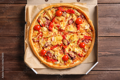 Cardboard box with delicious pizza on wooden table, top view