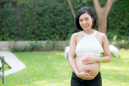 Beautiful pregnant of portrait asian young woman relax in the park, girl with belly standing on grass and yoga exercise for wellness, copy space.