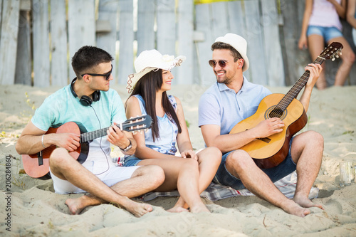 Young friends sitting on the beach and playing guitar © bokan