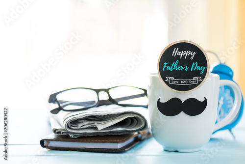 Happy fathers day concept. coffee cup with black paper mustache, heart tag with  Happy father's day text and newspaper, glasses on wooden table background. photo