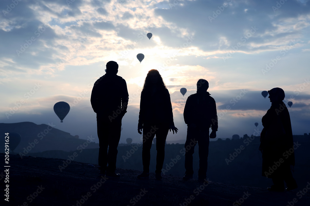 Silhouette of people looking at morning flight of passenger balloons in Cappadocia,