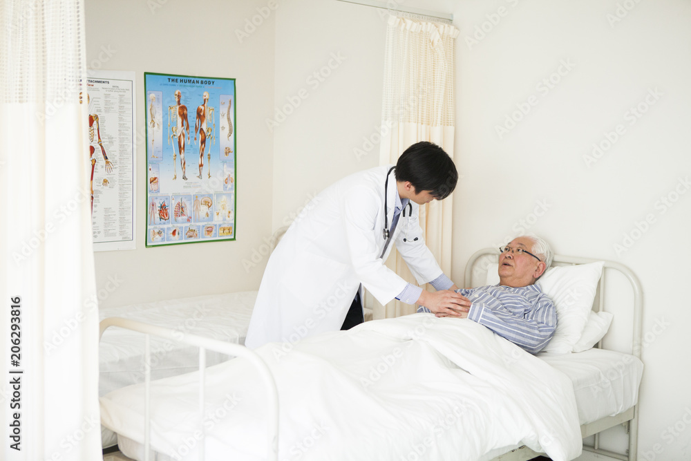 若い医師と、病室のベッドで横になっている高齢者の患者。 若い医師と、病室のベッドで横になっている高齢者の患者。