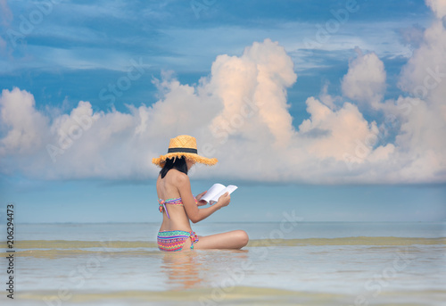 woman bikini lsitting in the sea water at lowest tide, enjoy reading book with beautiful sky and cleared water alone, relax and comfortable in holidays, vacation in summer time photo