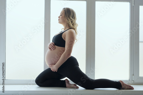 Young pregnant girl doing fitness on window sill