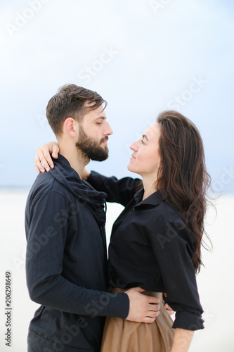 Young happy couple hugging each other and standing in white winter background, woman wearing skirt and keeping hat. Concept of romantic love and seasonal photo session, feelings and relationship. photo