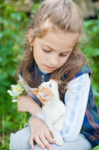 pretty little girl holding small cat on her knees looking each other in summer day