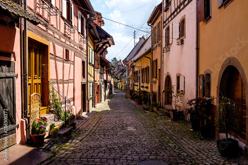 people walking along cobbled street between beautiful half-timbered houses in Eguisheim, Alsace