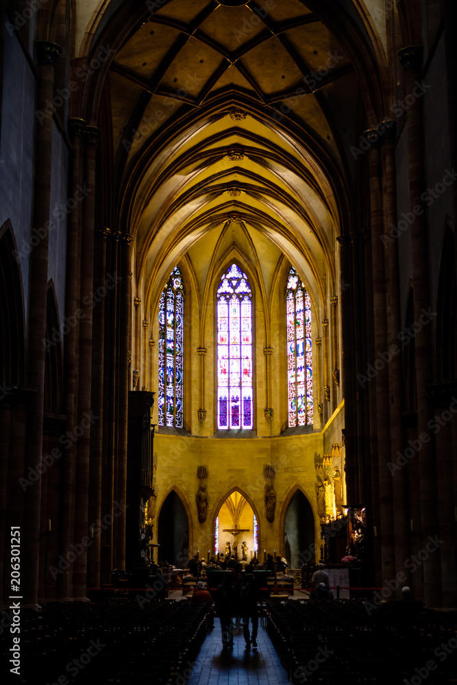 Two unidentified people walking along aisle in dark church. Kaysersberg, Alsace.