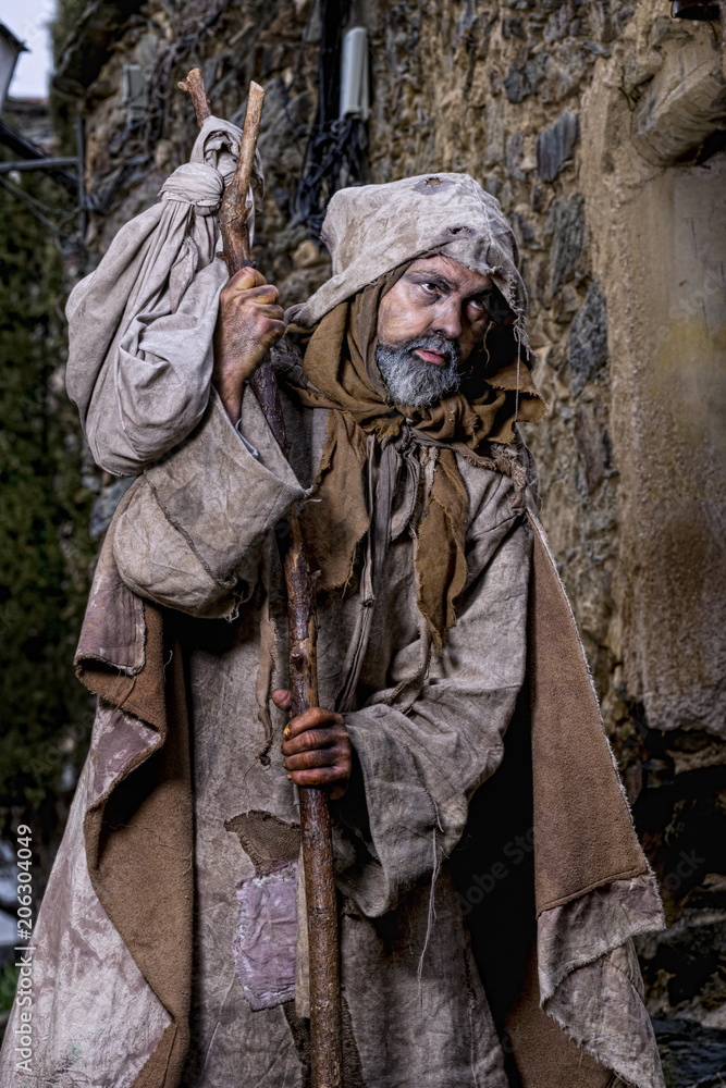 Man, dressed in rags, begging through the streets of a village