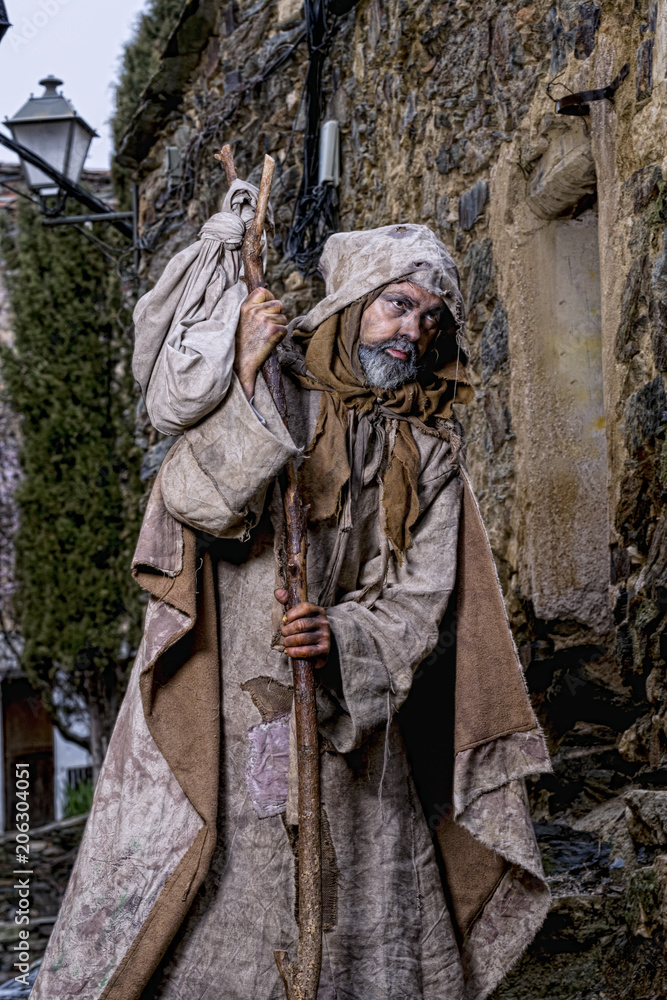 Man, dressed in rags, begging through the streets of a village