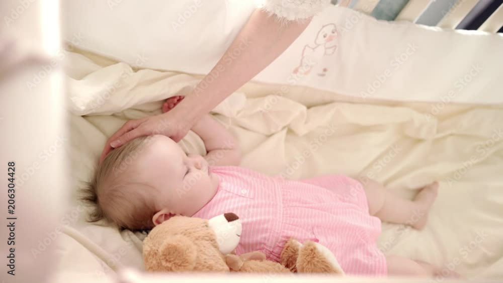 Baby sleep time. Sweet infant girl sleeping in crib. Mother hand stroking sleeping baby. Mother care. Toddler girl rest in cot. Little baby dream in crib. Adorable child resting with toy. Baby care Baby sleep time. Sweet infant girl sleeping in crib. Mother hand stroking sleeping baby. Mother care. Toddler girl rest in cot. Little baby dream in crib. Adorable child resting with toy. Baby care