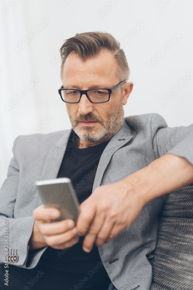 Mature man sitting on sofa with mobile phone Mature man sitting on sofa with mobile phone
