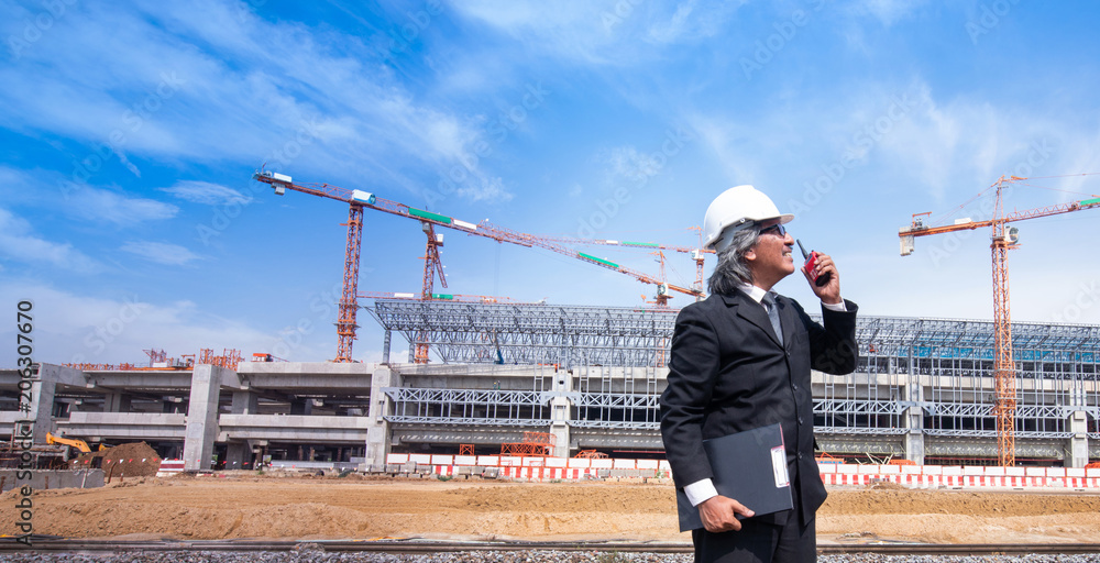 Asian business man with Walky Talky on construction site and tower cranes in background Asian business man with Walky Talky on construction site and tower cranes in background