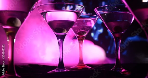 Alcohol drink poured into martini glasses of bottle. Several glasses of famous cocktail Martini, shot at a bar with dark toned foggy background and disco lights. Club drink concept
