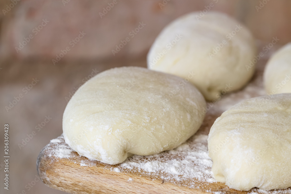 Raw homemade pies. Uncooked patties from yeast dough with stuffing are lying on a wooden plank and ready for baking. Closeup, selective focus, brick background Raw homemade pies. Uncooked patties from yeast dough with stuffing are lying on a wooden plank and ready for baking. Closeup, selective focus, brick background