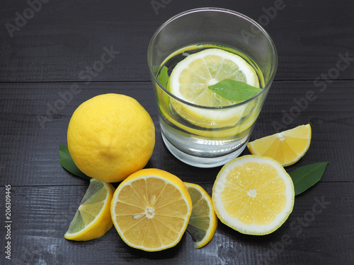 Fresh lemon juice in small bowl and lemon slice on dark wood background