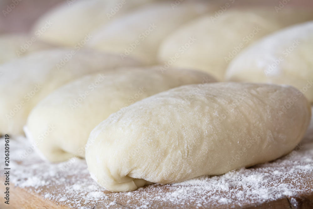 Raw homemade pies. Uncooked patties from yeast dough with stuffing are lying on a wooden plank and ready for baking. Closeup, selective focus, brick background Raw homemade pies. Uncooked patties from yeast dough with stuffing are lying on a wooden plank and ready for baking. Closeup, selective focus, brick background