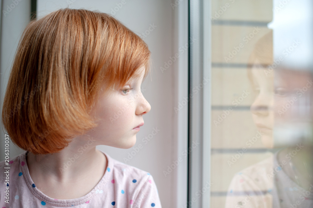 A girl looks into her reflection in a window