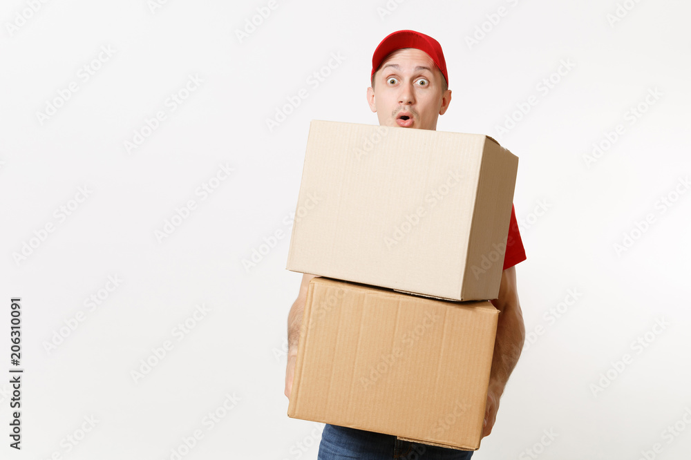 Delivery young man in red uniform isolated on white background. Male in cap, t-shirt, jeans working as courier or dealer holding empty cardboard boxes. Receiving package. Copy space for advertisement. Delivery young man in red uniform isolated on white background. Male in cap, t-shirt, jeans working as courier or dealer holding empty cardboard boxes. Receiving package. Copy space for advertisement.