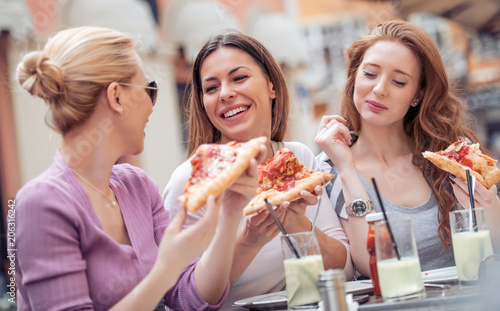 Portrait of three beautiful young women eating pizza after shopping