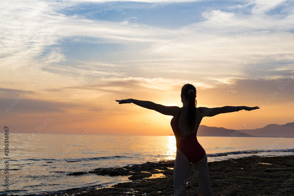 Silhouette healthy woman doing Yoga exercises on the beach in sunset time, Thailand