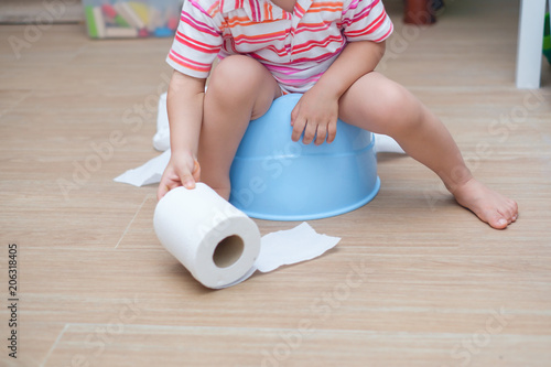 Quadro em tela Closeup of legs of little Asian 2 years old toddler baby boy child sitting on blue potty holding, playing with toilet paper
