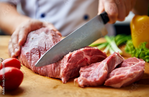 Portrait of chef hands cutting raw meat on wooden desk. 