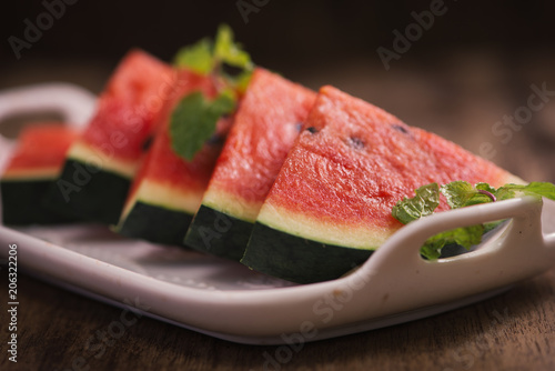 Fresh sliced watermelon in white dish on wooden table.