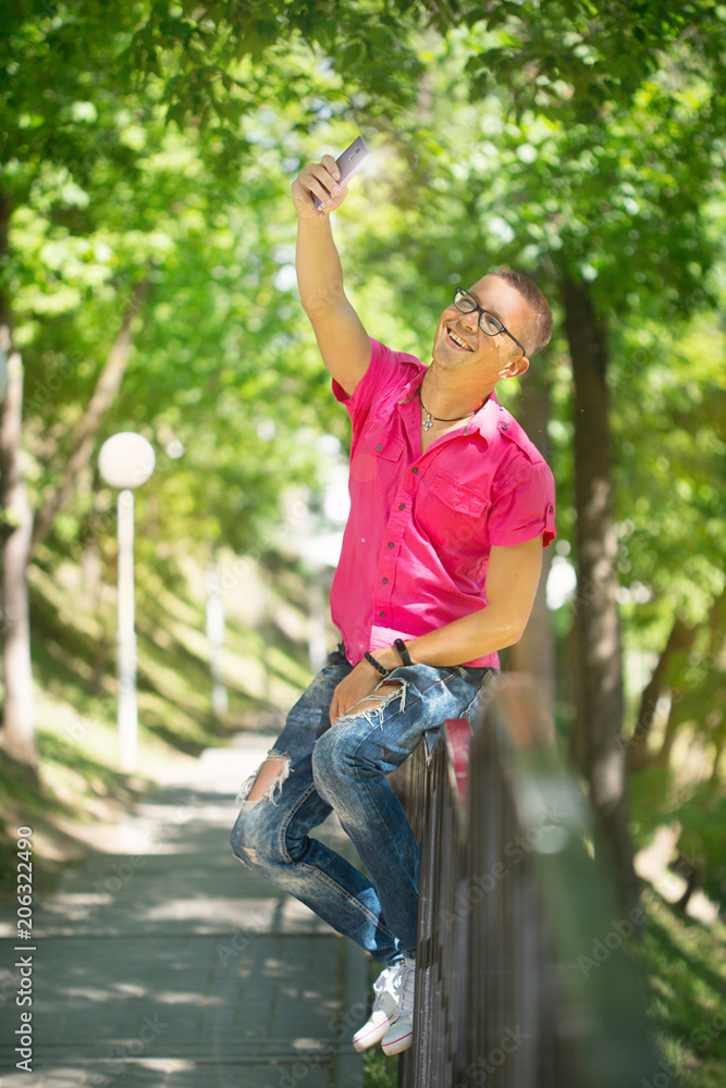 Cute emotional man with headphones wearing glasses in a pink shirt, walking with the phone. Selfie. the man is talking on the phone Cute emotional man with headphones wearing glasses in a pink shirt, walking with the phone. Selfie. the man is talking on the phone