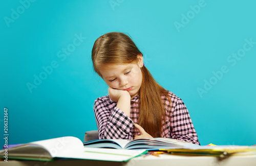 Fotografie Tired girl in weary state reads book at her desk and experiences dissatisfaction