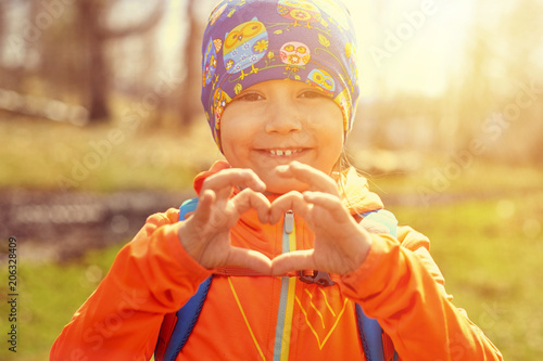 little happy girl with backpack making heart of her hands close-up. Outdoor portrait photo