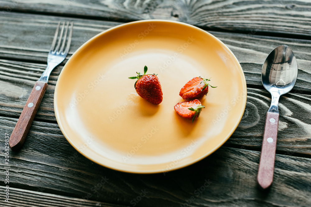 Red strawberries served on plate with spoon and fork on wooden table Red strawberries served on plate with spoon and fork on wooden table