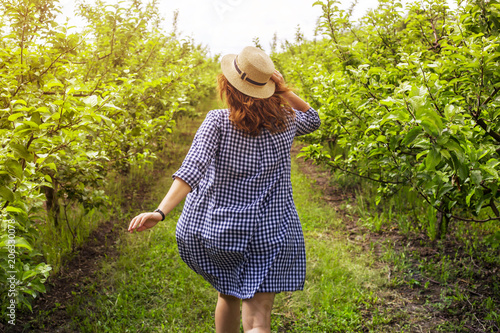 A gardener girl runs through a green apple orchard in a blue dress and hat © svitlini