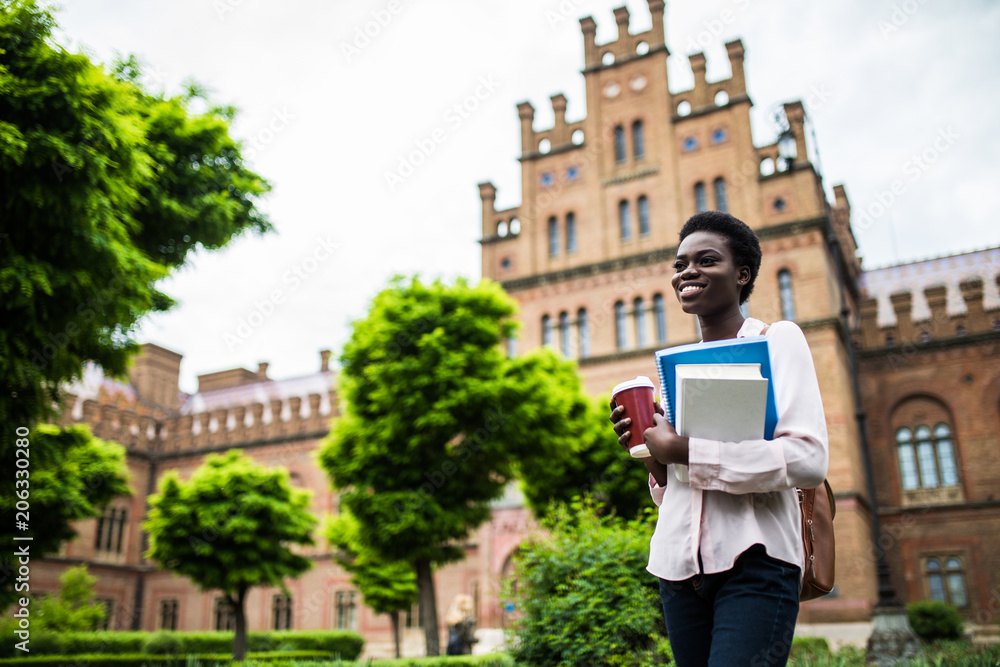 Young group of students with backpacks and books with Campus as a background. Afro American girl with notebooks and cup of coffee looking at camera. Young group of students with backpacks and books with Campus as a background. Afro American girl with notebooks and cup of coffee looking at camera.